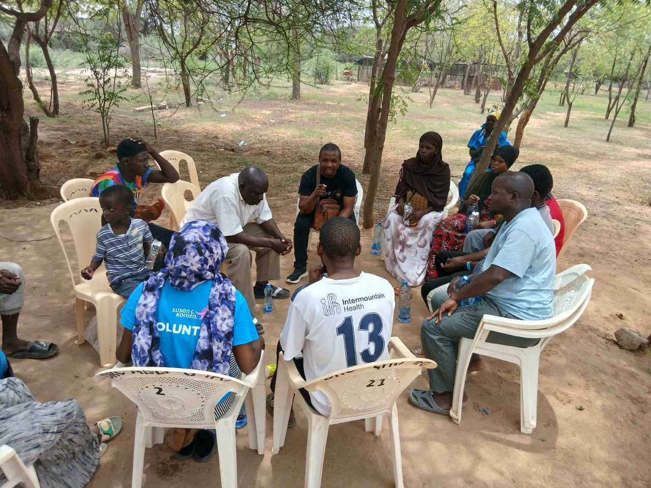 Community members seated in a circle under trees during a GHEA community meeting in Dadaab