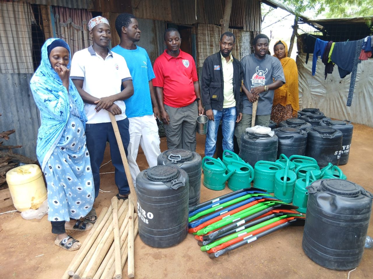 GHEA members standing with watering cans, water containers, shovels and farming tools